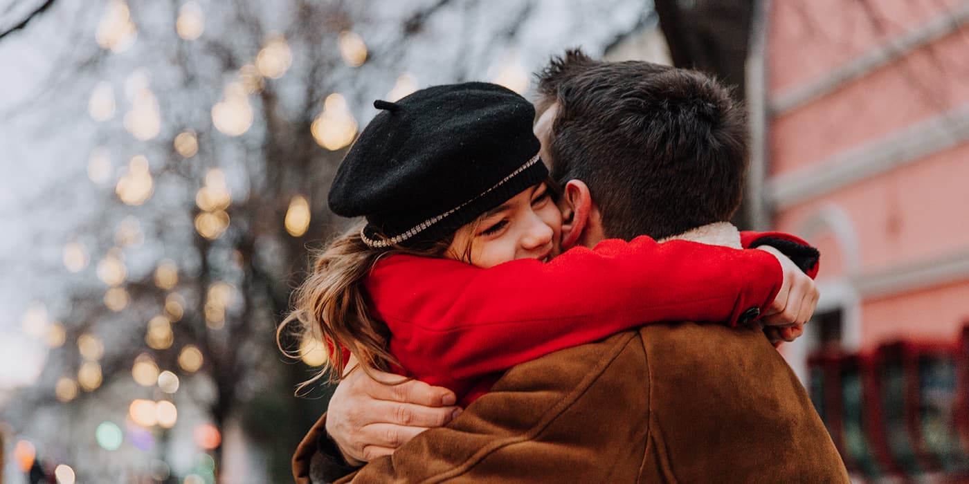A young girl embracing her dad at an outdoor shopping center.